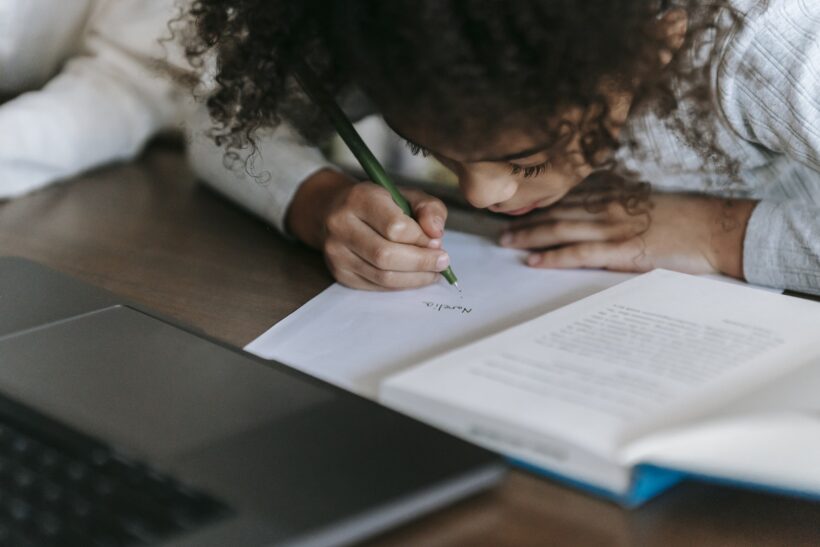 Black girl writing on paper while reading book
